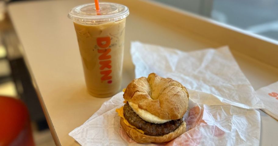 A dunkin iced coffee and sausage egg and cheese on a croissant