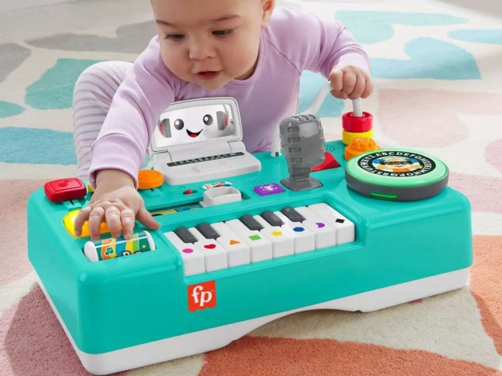Baby sitting on the floor playing with a Fisher Price DJ table.