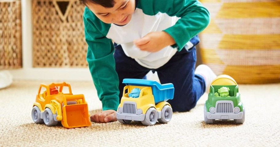 boy playing with 3 green toys construction trucks on carpet