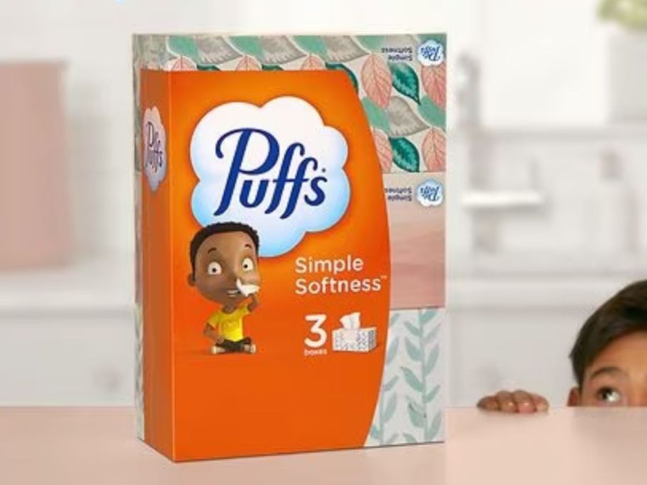 3 pack of Puff's Simple Softness Tissues on counter with little boy peeking a look