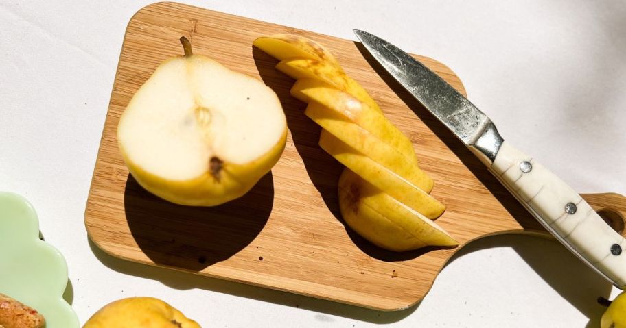 A cutting board with a Harry & David pear cut in half next to slices of pear and a knife