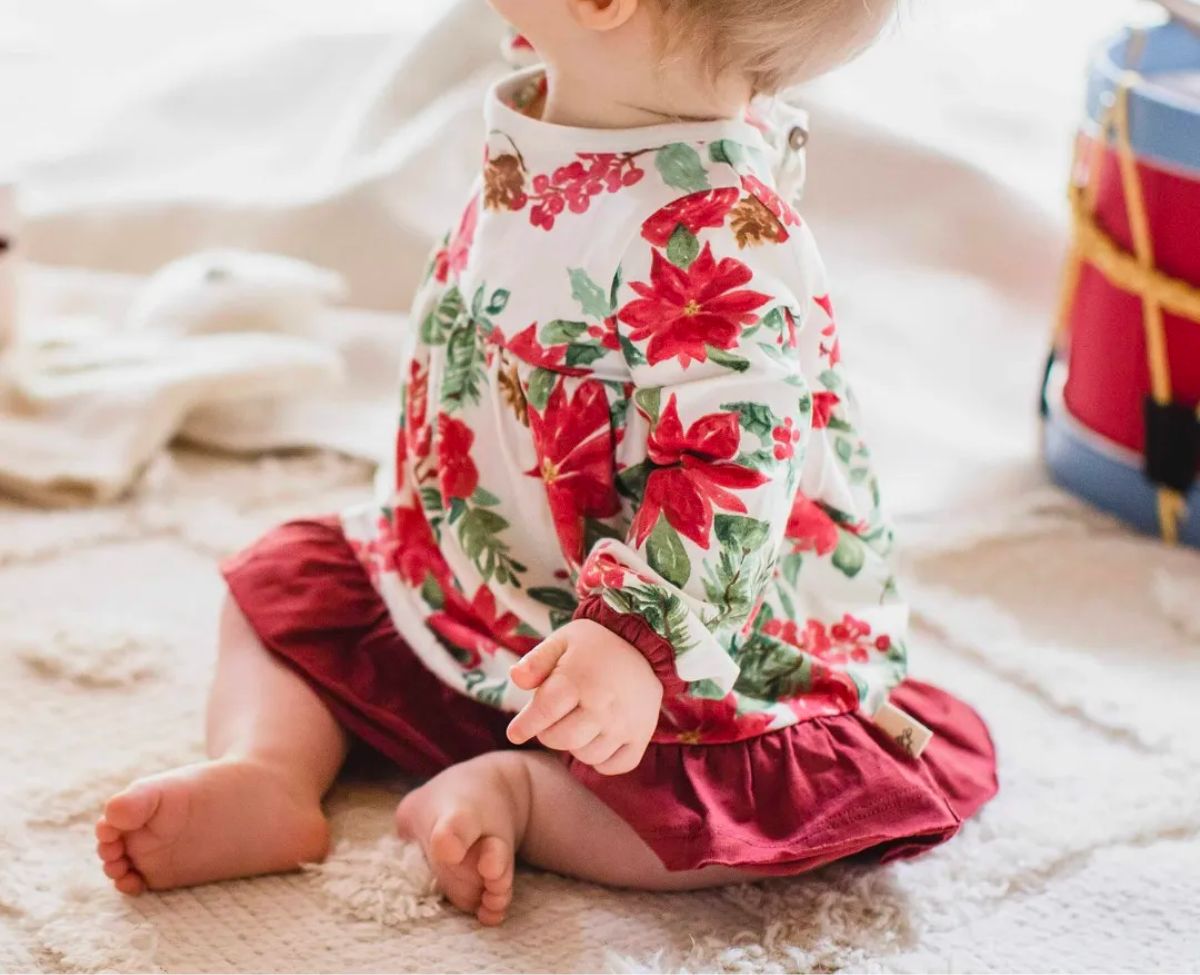 a baby sitting on the floor wearing a Holiday Floral Organic Cotton Dress