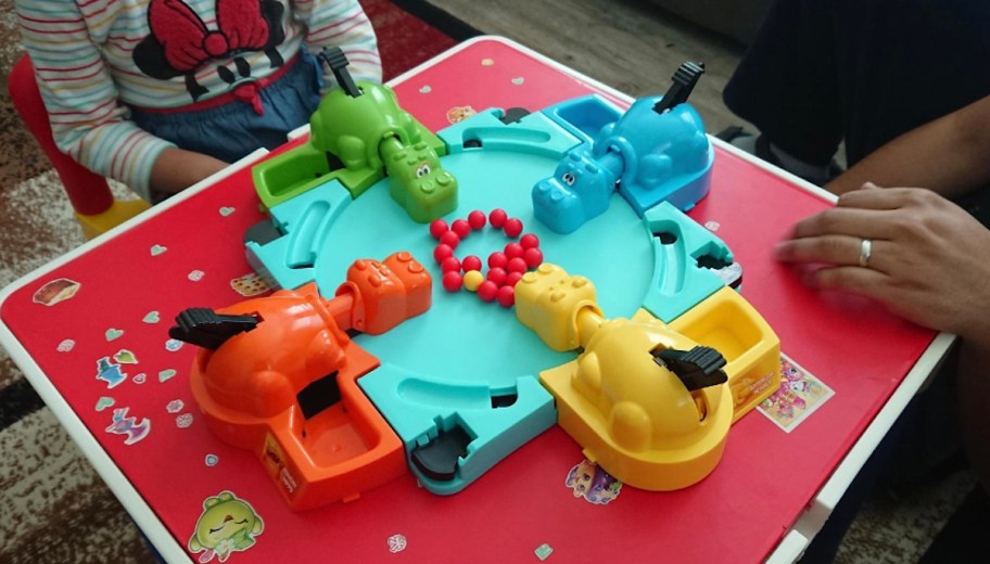 People sitting around red table with hungry hungry hippos board game