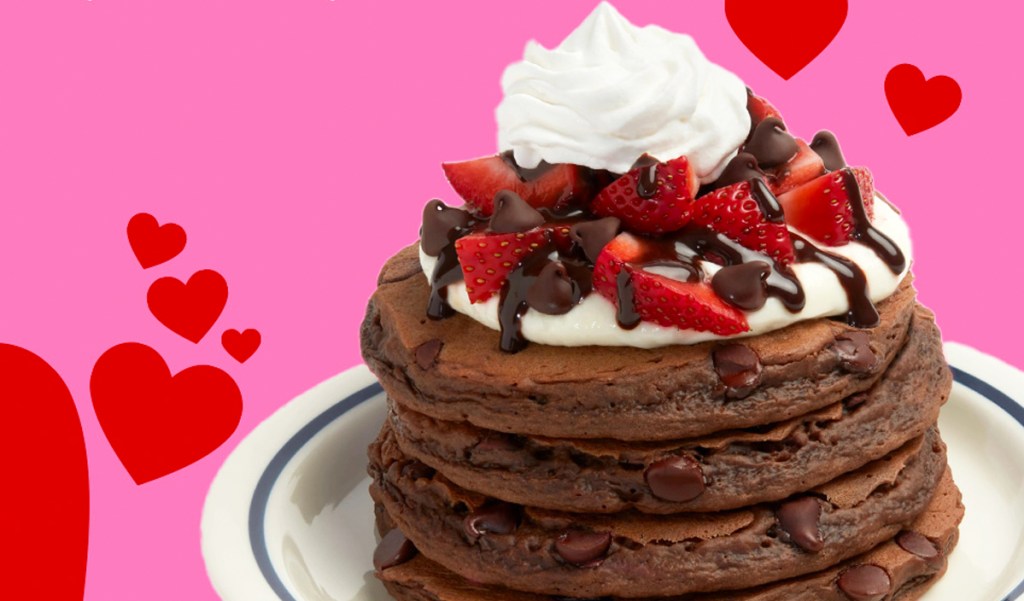 stack of chocolate pancakes with strawberries, chocolate, and whipped cream on top