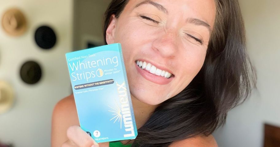 Woman holding a box of Lumineux Whitening Strips next to her bright smile