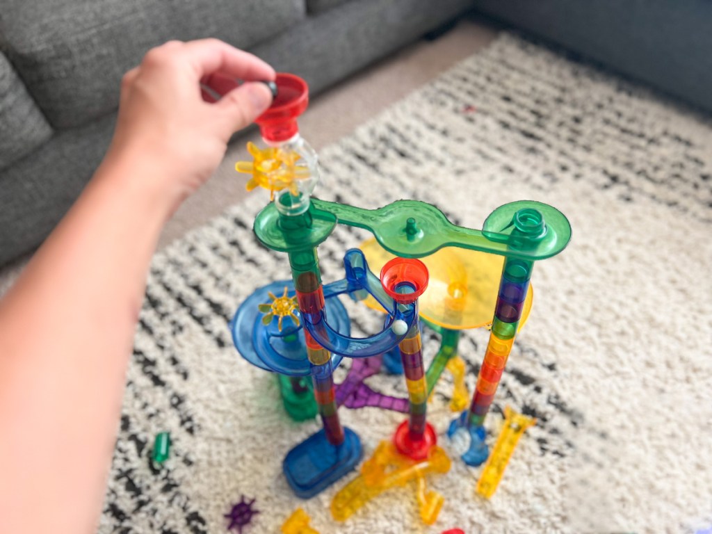 Hand putting marble in assembled and colorful cool toys marble run on rug in living room