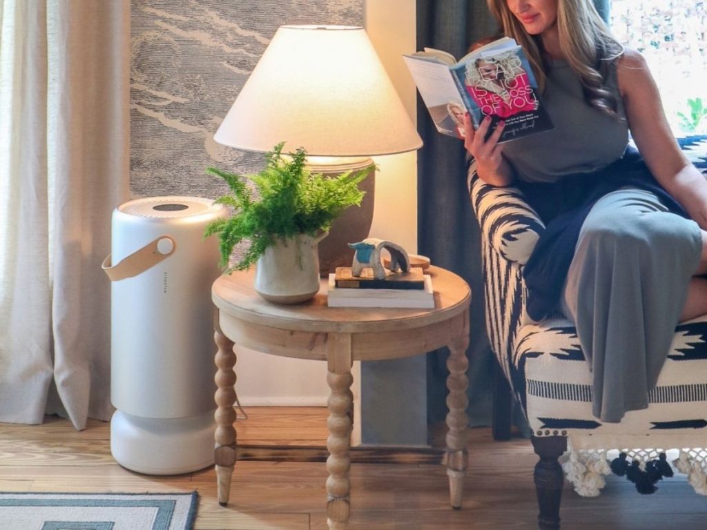 Woman sitting on a couch reading a book with a molekule ait purifier nearby