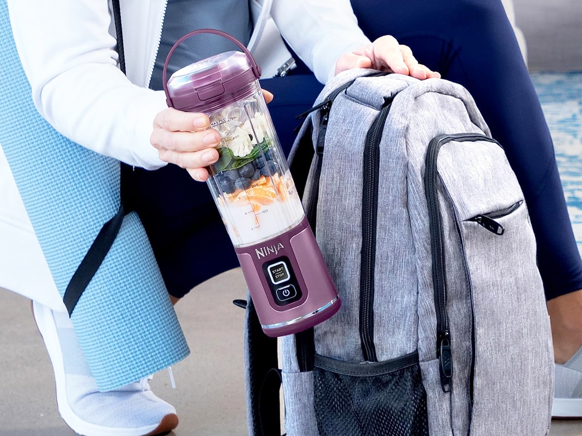 woman placing a purple ninja personal blender into backpack