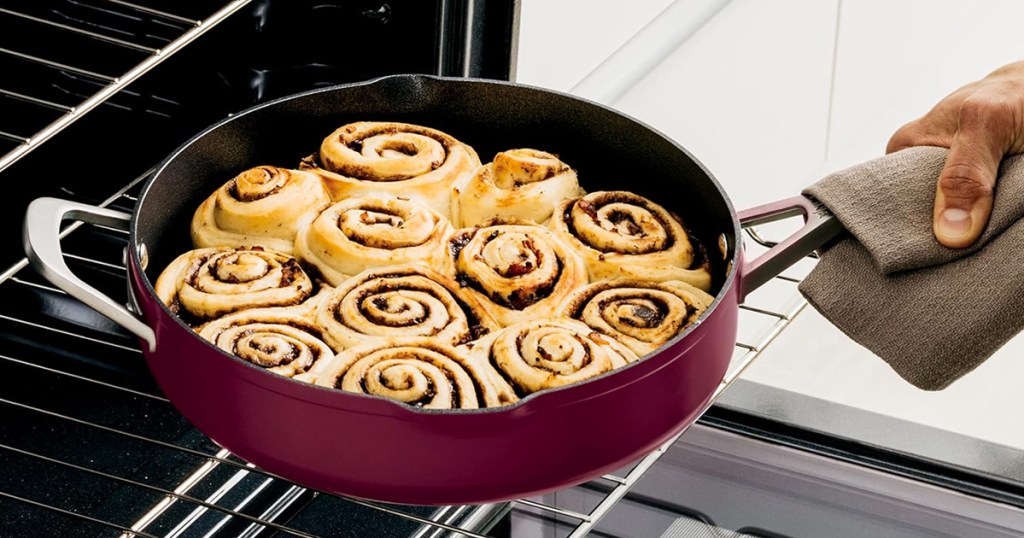 hand grabbing pan filled with cinnamon rolls from oven