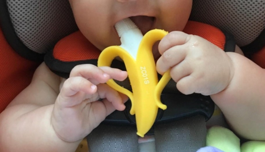 baby in car seat holding banana shaped teether in mouth 