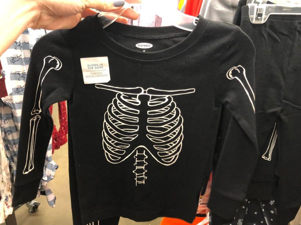 Hand holding a hanger with Old Navy Skeleton pajamas for kids
