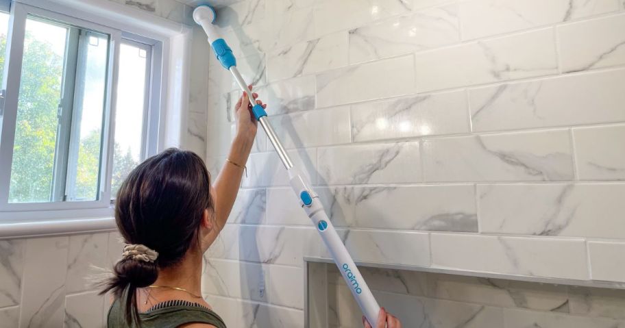 woman using blue and white scrubber brush on wall of bathroom