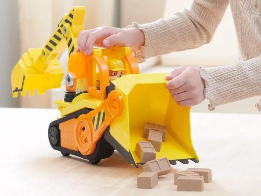 Girl's hands playing with the PAW Patrol Rubble & Crew Rubble Deluxe Bulldozer Toy Vehicle