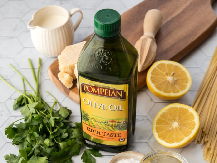 Pompeian Olive Oil bottle next to a cutting board, lemons, parmesan, pasta, and parsley