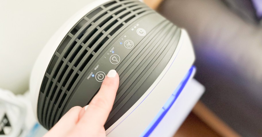 finger pressing button on top of air purifier