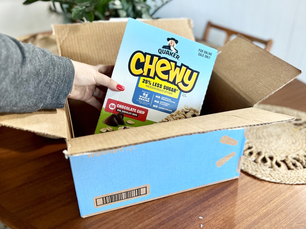 hand grabbing a large box of quaker chewy bars out from a walmart shipping box