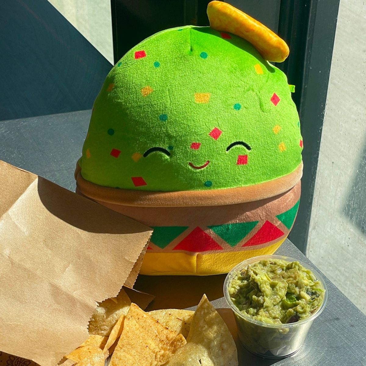 Squishmallow that looks like guacamole next to chips and guac