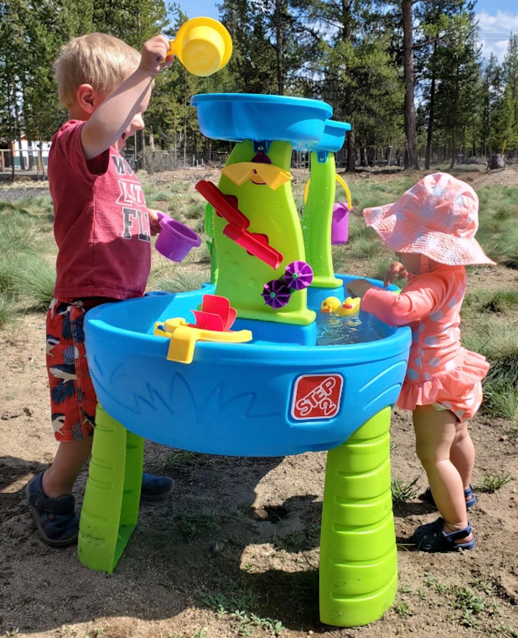two kids standing at blue and green water table outside in grass