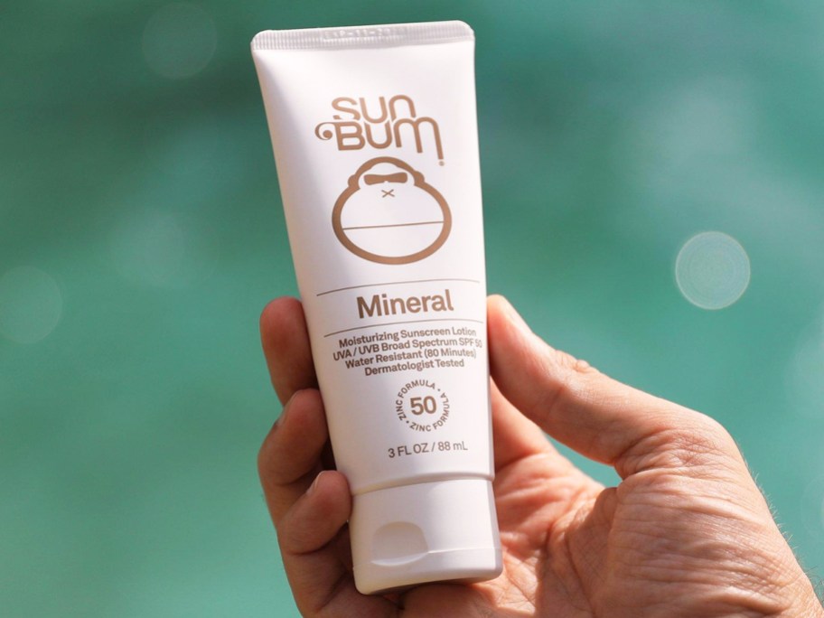 hand holding a white tube of Sun Bum Mineral SPF 50 Sunscreen Lotion 