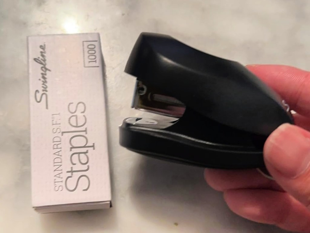 Person holding black mini stapler next to box of staples