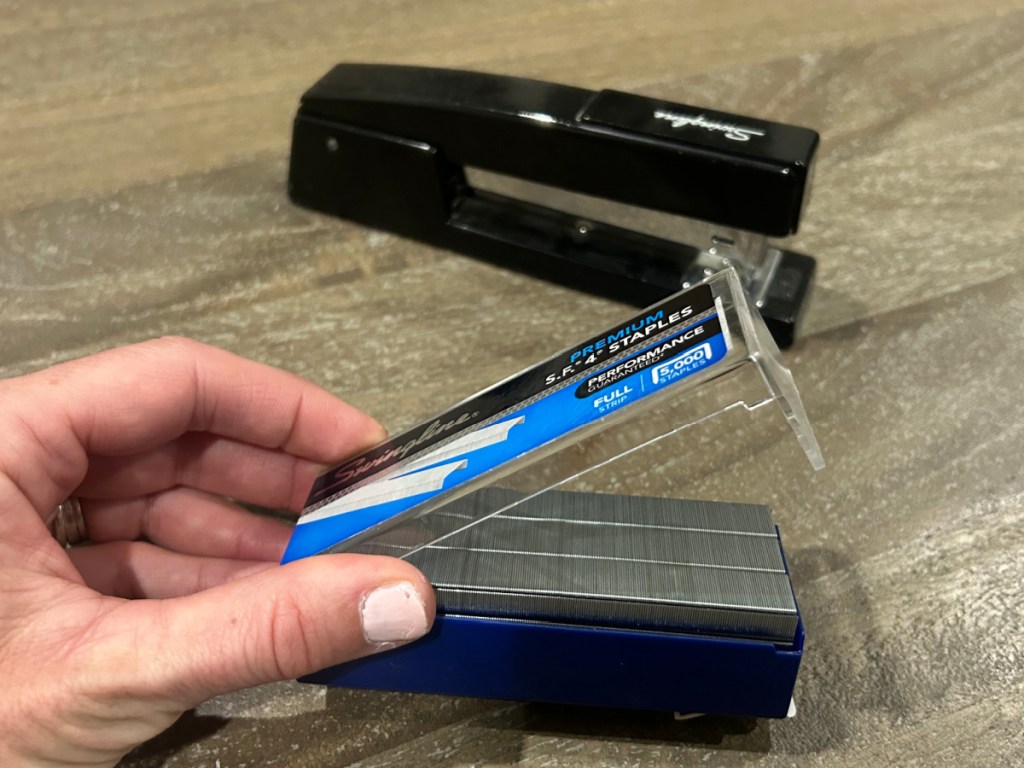person opening up swingline staples box on table next to stapler