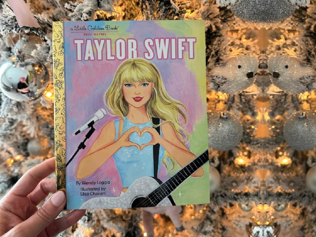 person holding Taylor Swift Golden Book in front of christmas tree