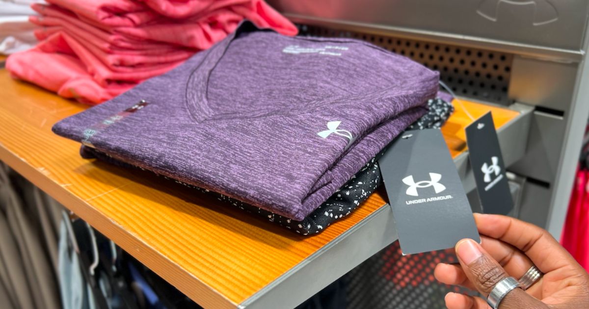 a womans hand displaying the tag attached to an Under Armour women's shirt