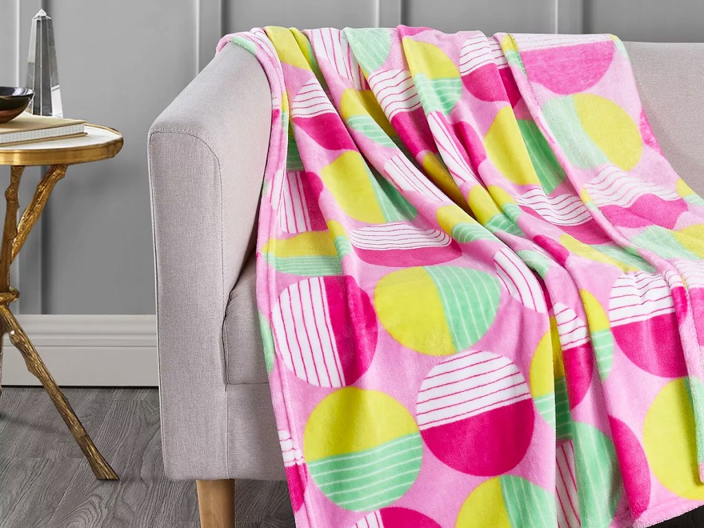 pink, yellow, and green throw blanket with circle print draped over grey couch