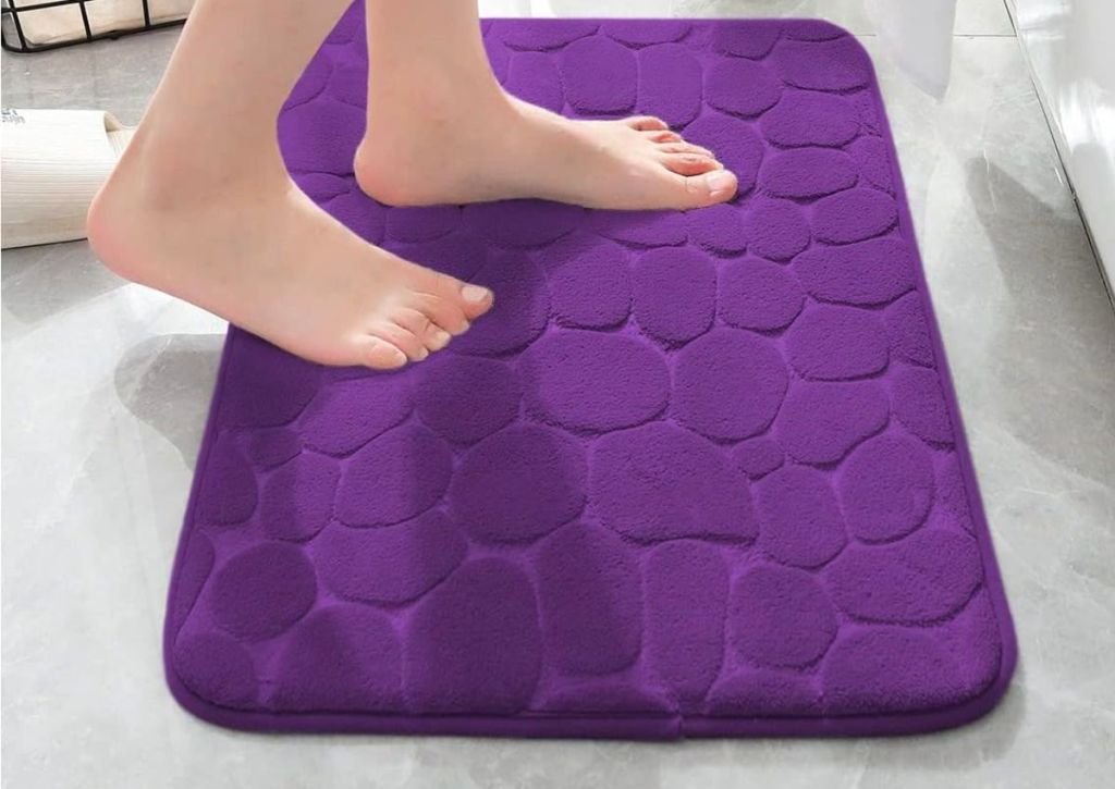 a womans feet stepping on to a YIHOUSE Memory Foam Cobblestone Bath Mat in eggplant