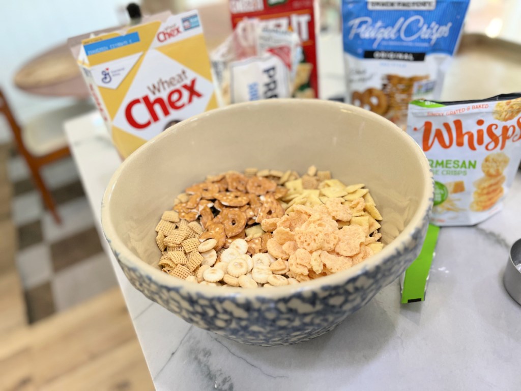 adding chex and snack crackers to a large bowl