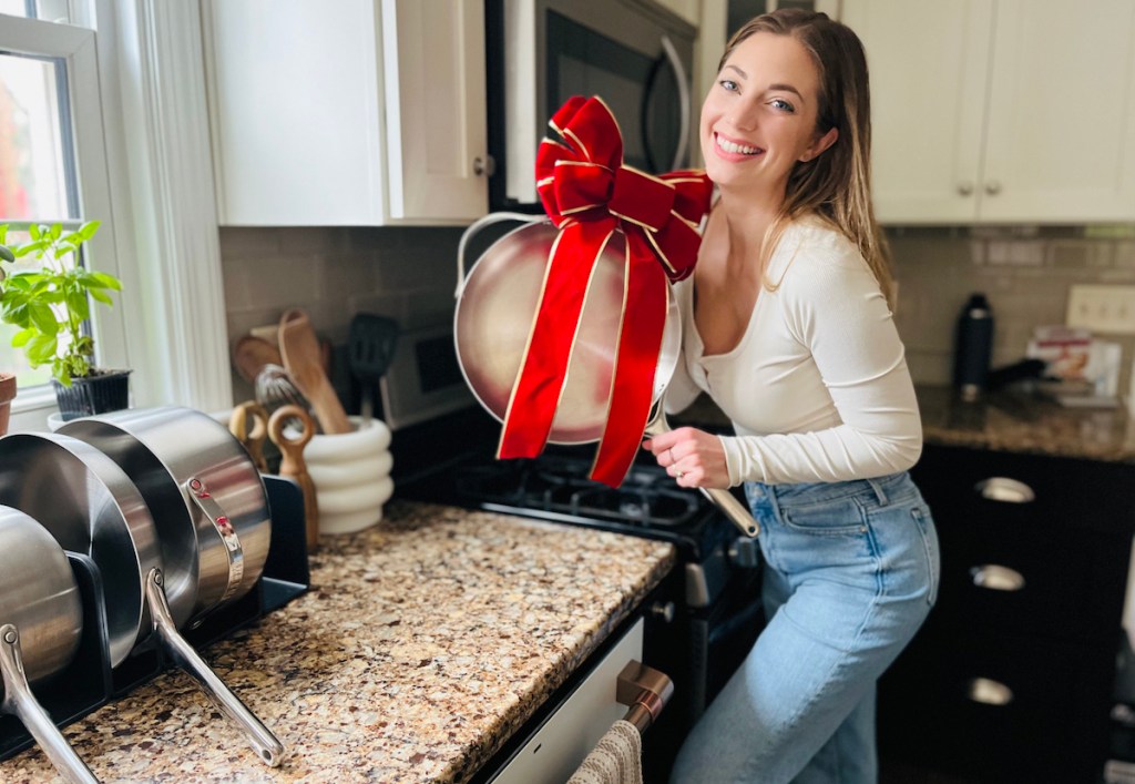 Woman holding stainless steel pan with big red bow standing in the kitchen 