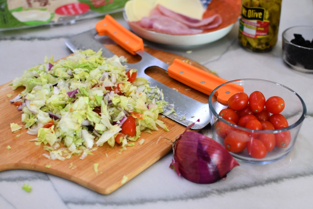 chopping lettuce with tomatoes and red onion on a large cutting board
