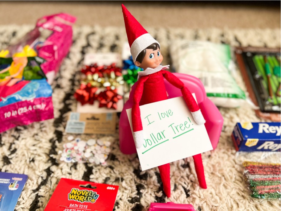 elf holding dollar tree sign in front of supplies for dollar tree elf on a shelf ideas