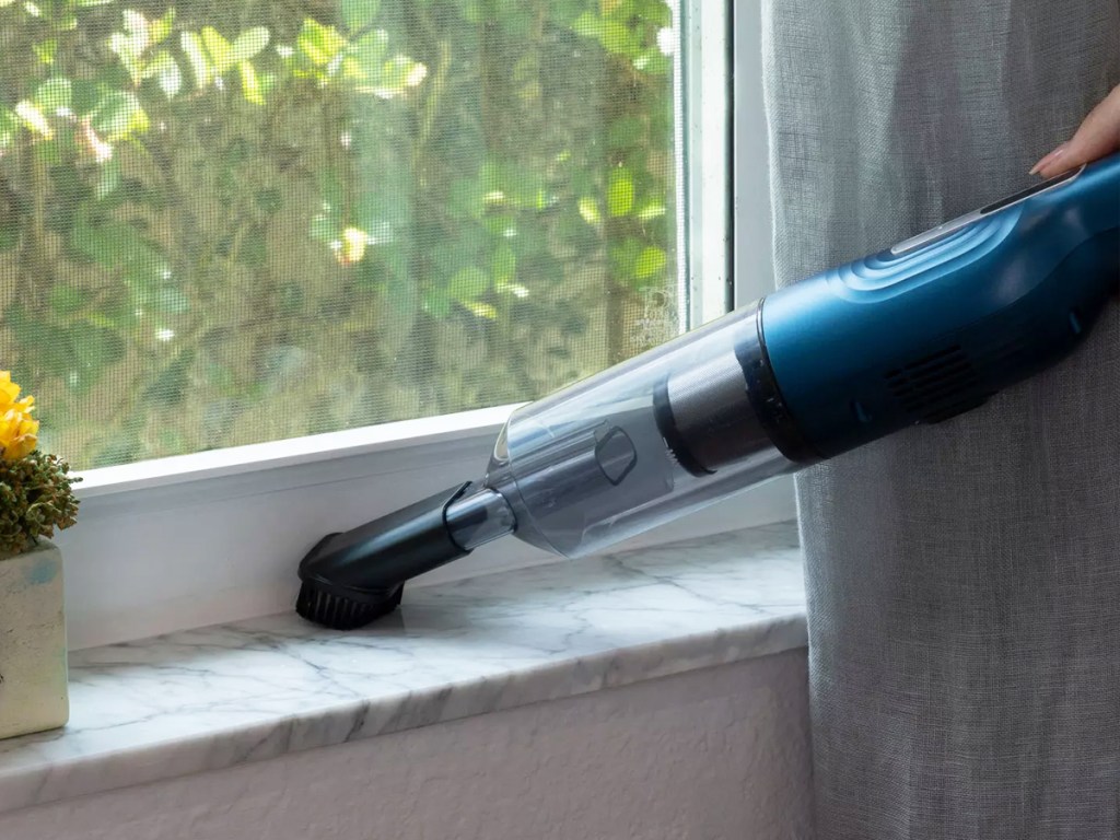 using blue and grey cordless mini vacuum on windowsill 