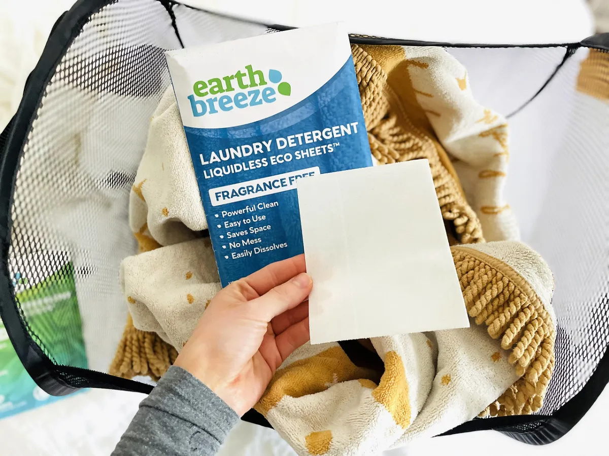 womans hand holding an earth breeze laundry sheet over a package of the sheets and some laundry