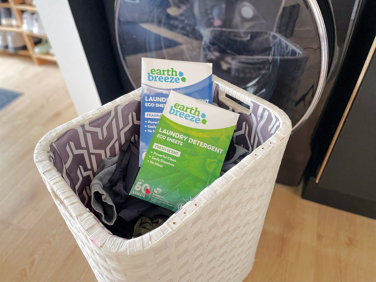 packages of earth breeze laundry sheets in a clothes hamper in front of a washing machine