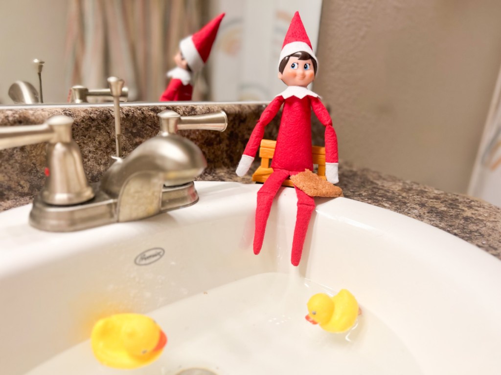 elf sitting on sink feeding rubber ducks