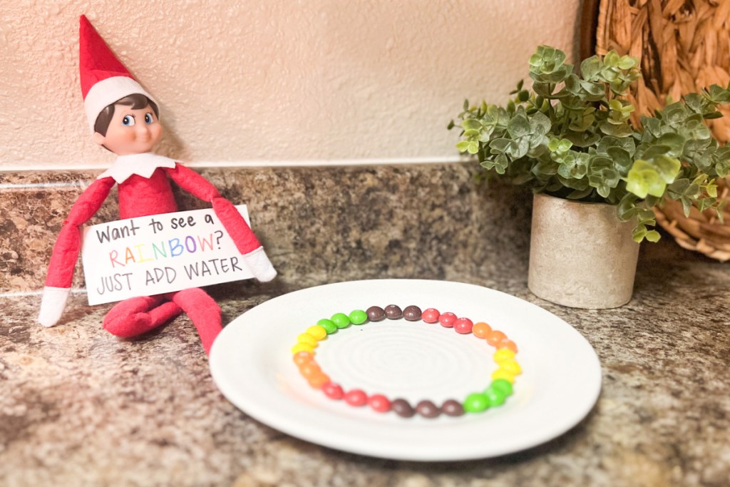 elf sitting next to plate of skittles