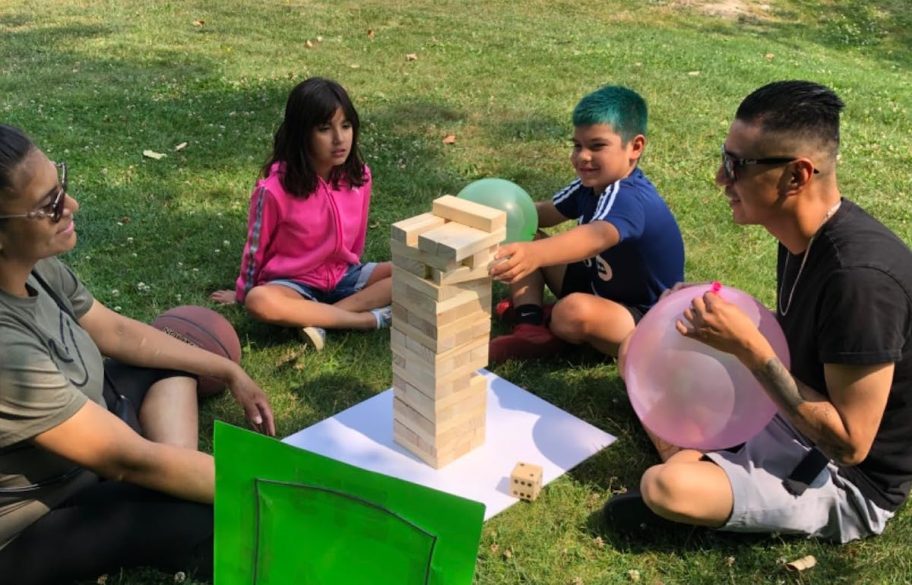family sitting in grass playing giant tumbler tower game
