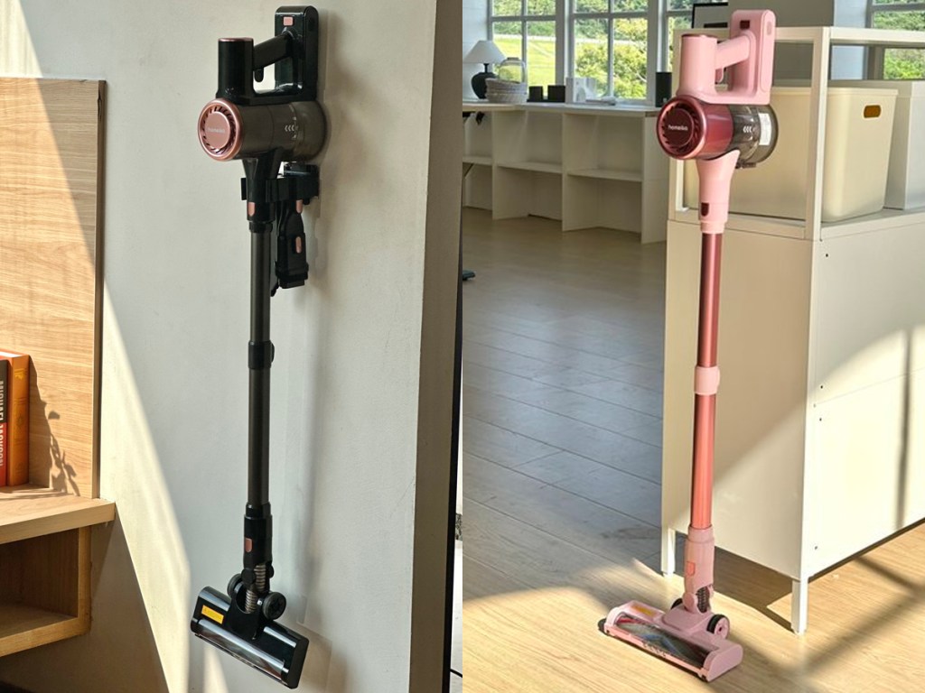 black cordless vac hanging on wall and pink stick vac standing in kitchen