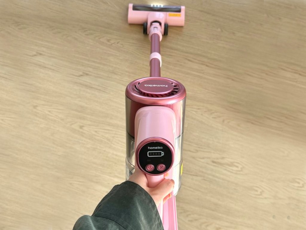 woman using pink cordless stick vacuum on hardwood floor