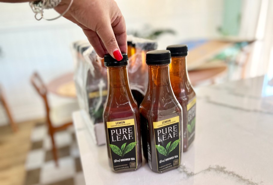 hand touching the cap of a bottle of pure leaf tea sitting on a counter with other bottles
