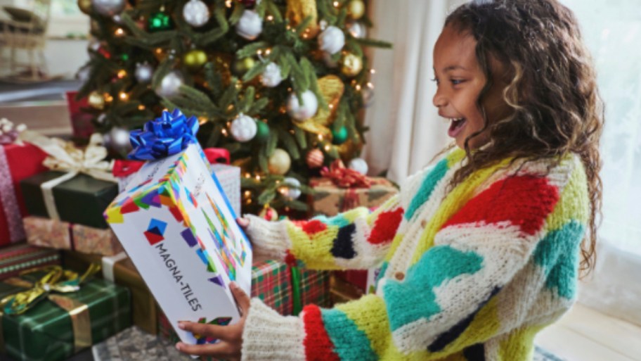 girl holding box of magna tiles in front of christmas tree
