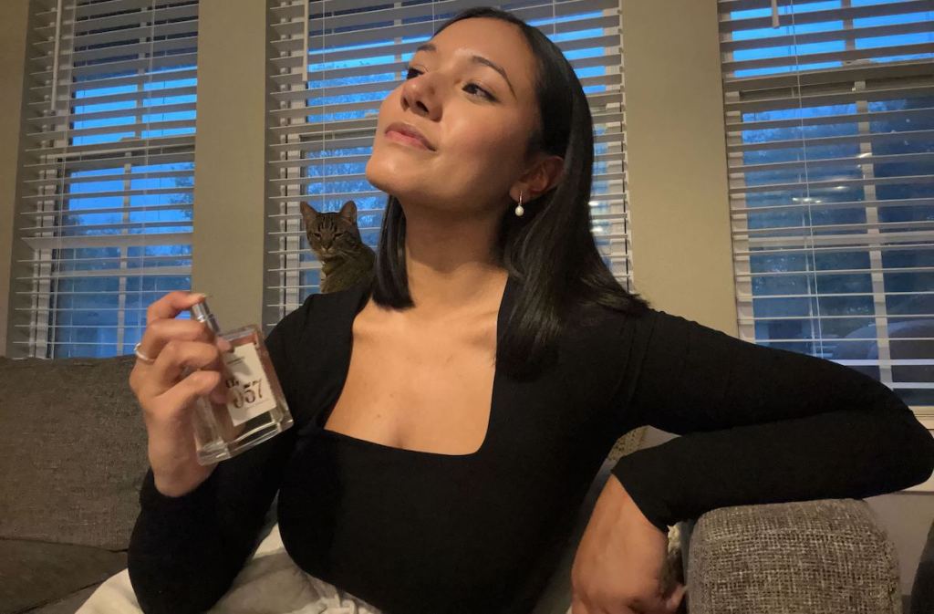 Woman sitting on couch spraying perfume on neck 
