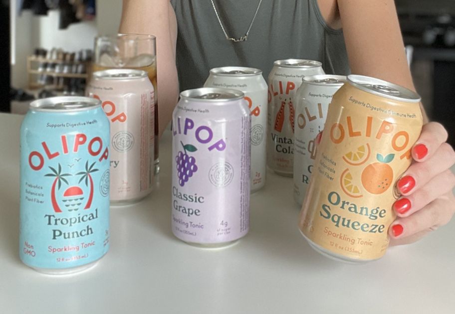 woman standing behind several different flavors of Olipop sodas on a kitchen counter, with her hand on 1