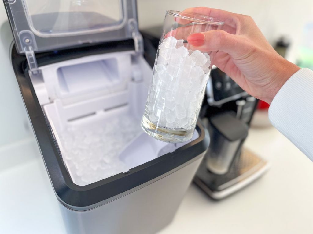 person holding a glass filled with ice in front of ice maker
