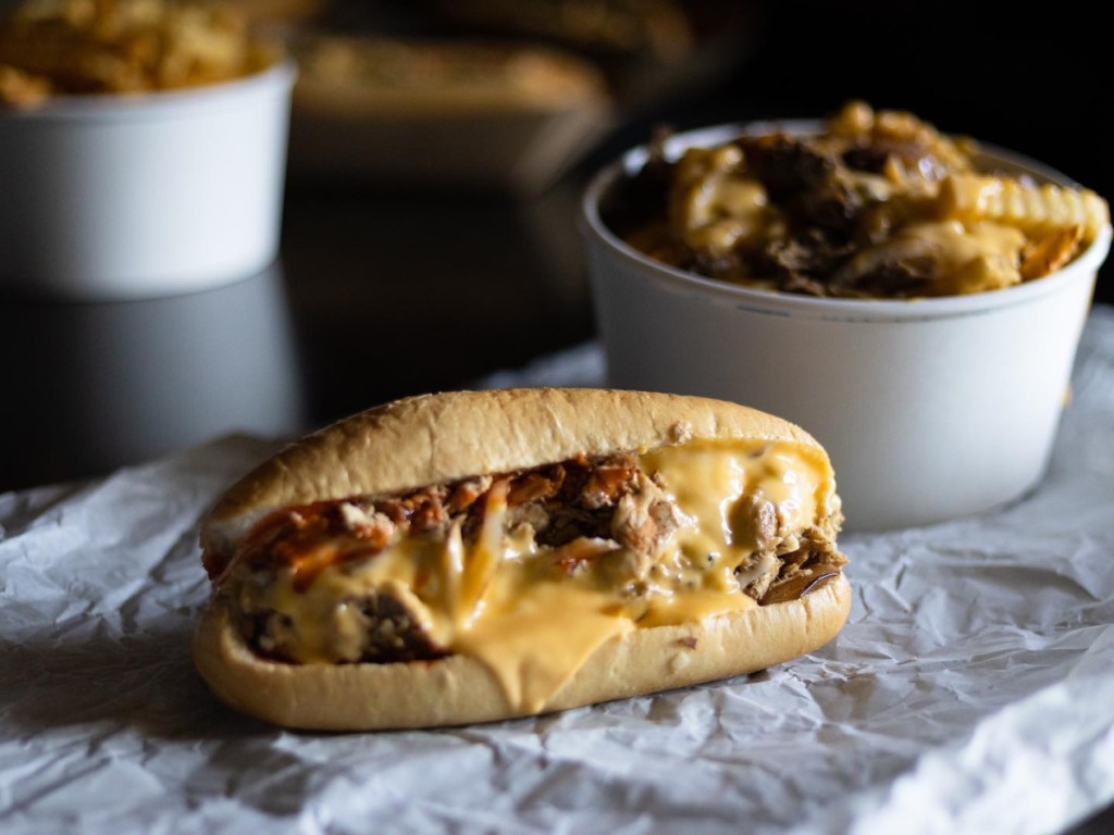 professional photo of a cheesesteak on a wrapper near containers of fries