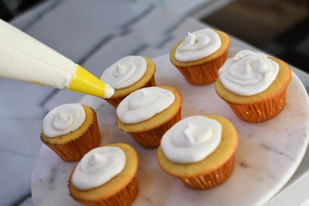 piping on buttercream frosting to cupcakes