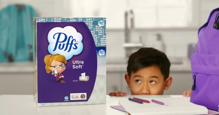child peeking at a package of puffs tissues from behind a kitchen counter