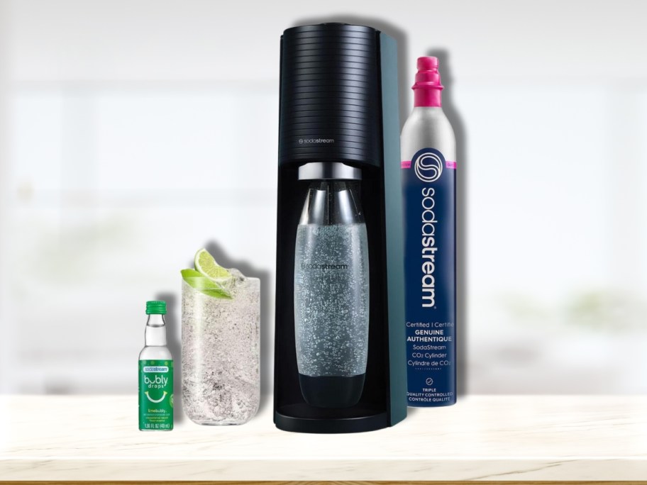 black Sodastream machine with CO2, glass of soda and Bubly flavor bottle on a counter